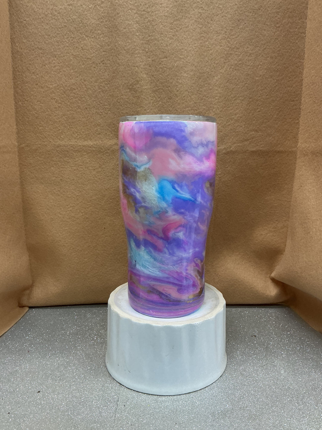 Hand-painted ceramic vase with dark pastel swirls in pink, purple, blue, and gold, displayed on a white pedestal against a brown background.