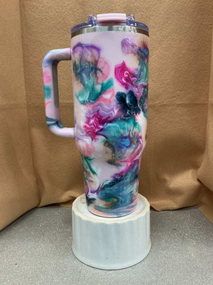 Big Swig tumbler with a colorful marbled design in pink, purple, blue, and black, featuring a handle and a pink lid, displayed on a white stand.